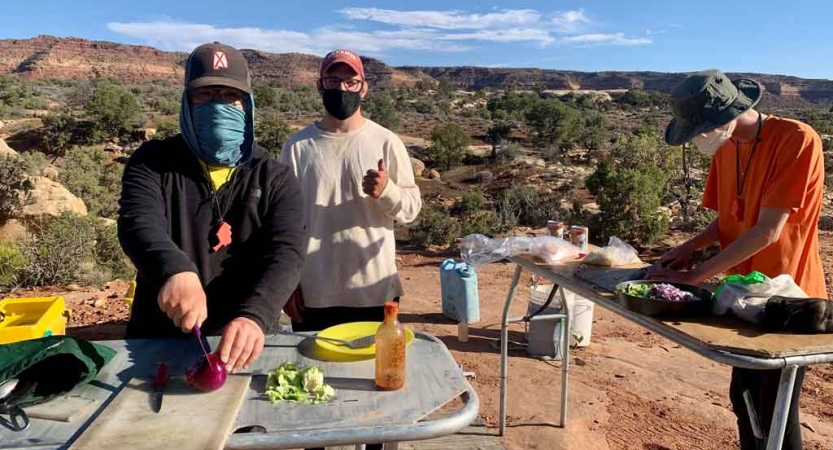 Three people prepare food on tables outdoors.